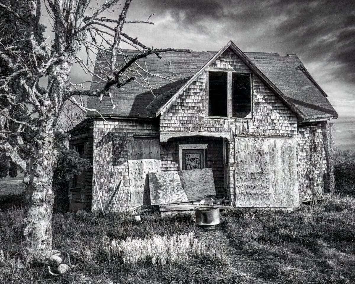 A black and white rural photograph of an abandoned shingled house in rural Grays Harbor County, Washington.