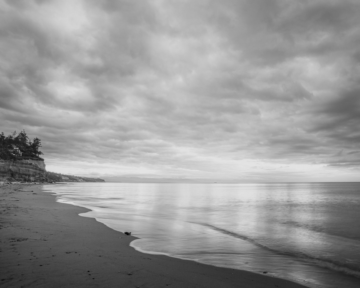 Under the brooding early autumn skies, the serene West Beach on Whidbey Island, Washington, unveils a dance of light and shadow. The monochromatic tones capture the tranquil yet dramatic atmosphere, where the clouds converse with the gentle waves. Amidst this natural spectacle, one finds a moment of introspection and awe.