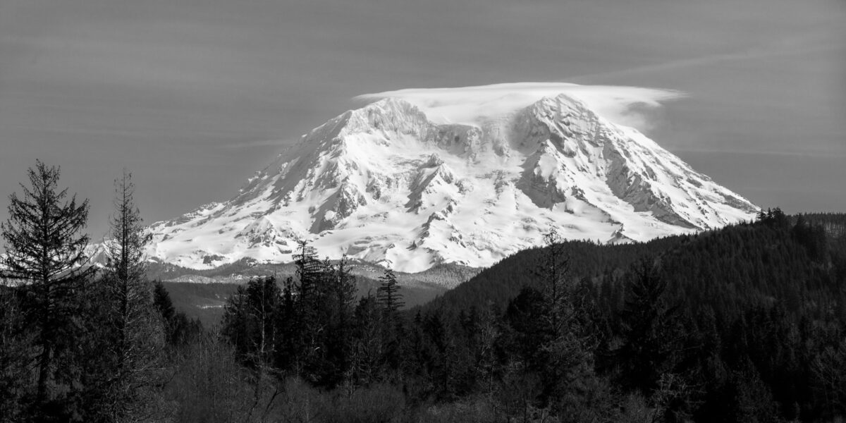 A black and white landscape panoramic photograph of a snow covered Mt. Rainier in Washington.