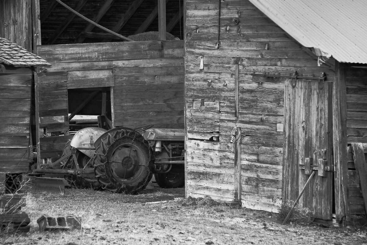 A black and white photograph of an old barn and tractor off of Riverbottom Rd. in Kittitas County near Ellensburg, Washington.