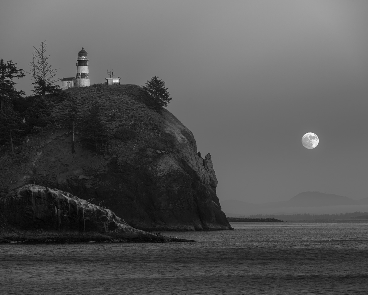 As the longest day gives way to the twilight of the Summer Solstice, I stand at Cape Disappointment State Park in Washington State, capturing the serene ascent of the moon. Its ethereal glow breathes life into the monochrome landscape, casting a gentle luminescence on the stoic lighthouse. At this moment, time stands still, and the solstice moonrise etches a memory of tranquil harmony between Earth and the cosmos.