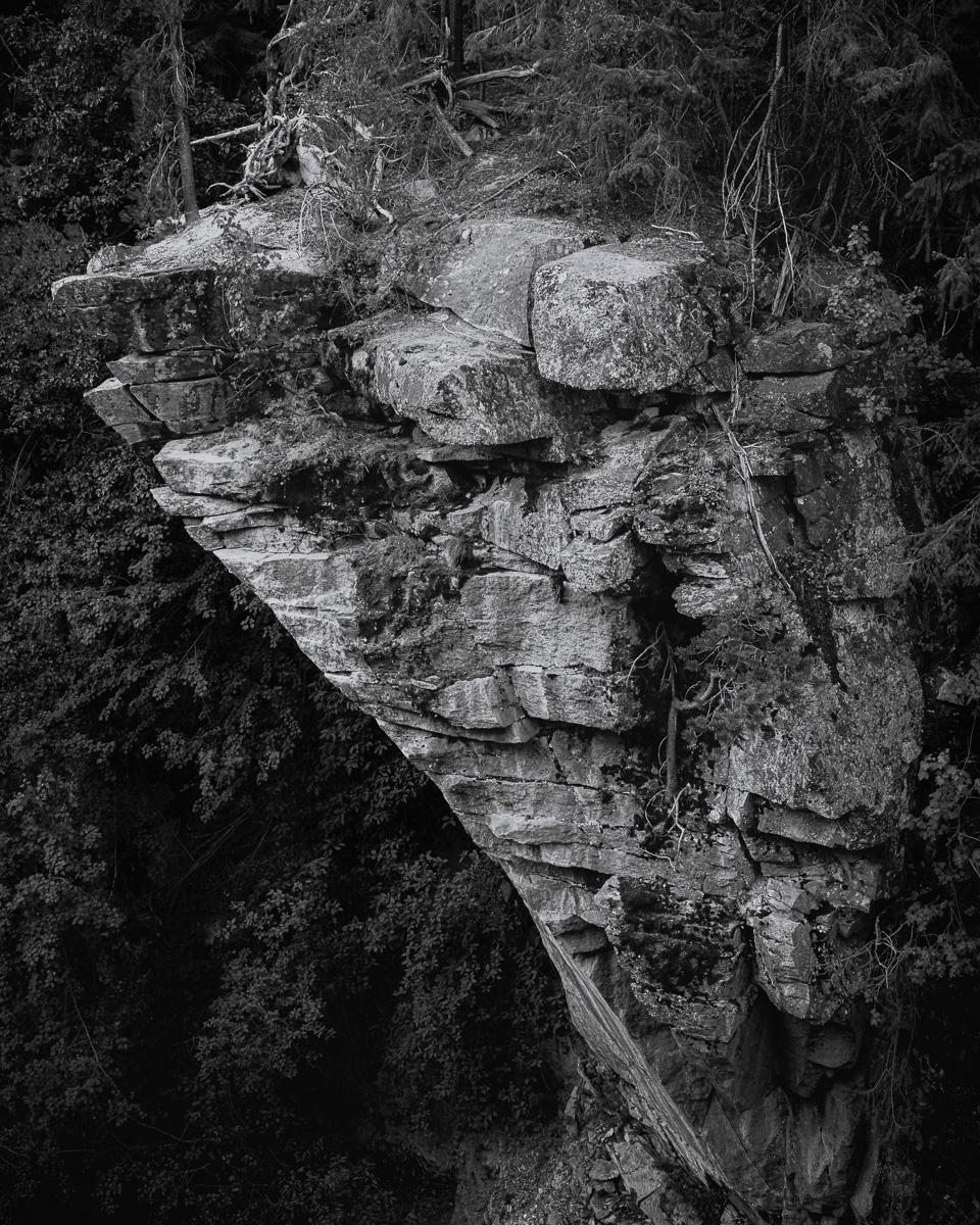 Defying gravity and time, this monolithic cliff face is a testament to the raw power of the Box Canyon's geological forces. Etched by millennia of wind, water, and weather, its layered facade tells a story of endurance and transformation. This black-and-white image's stark contrast between light and shadow accentuates the rugged textures and intricate patterns carved into the rock. At the same time, hints of vegetation cling tenaciously to its surface, showcasing nature's resilience. This imposing structure, overlooking the Entiat River below, is a silent witness to the ceaseless flow of water and time through this ancient landscape.