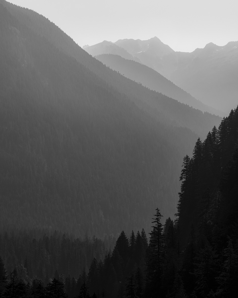 Layers of mountains stretch into the distance, their forms softened by a thick haze of wildfire smoke. The Cascade River Valley's stillness feels tranquil and haunting as the smoky air cloaks the ridges in a mysterious veil. This scene captures the quiet resilience of Washington's North Cascades amidst nature's raw elements.