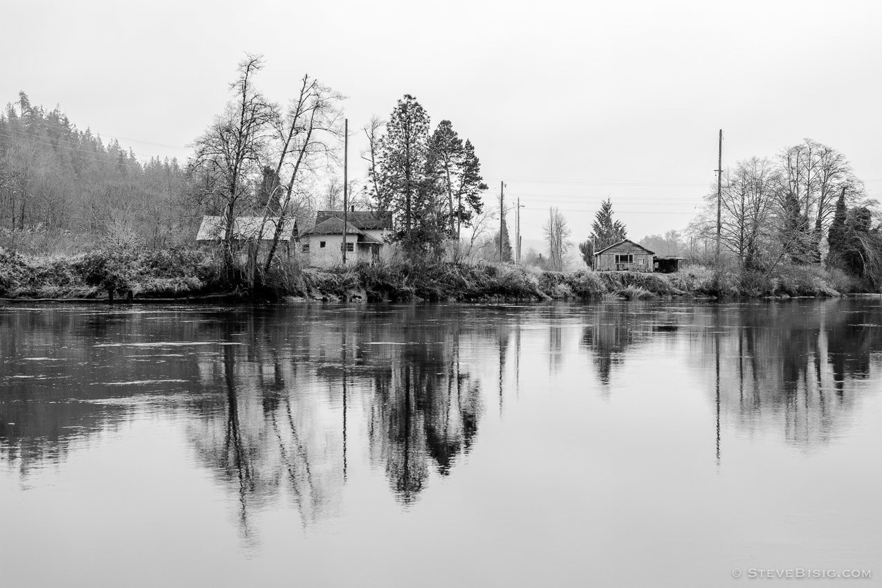 A black and white photograph of several abandoned houses from across the Chehalis River near Montesano, Washington.
