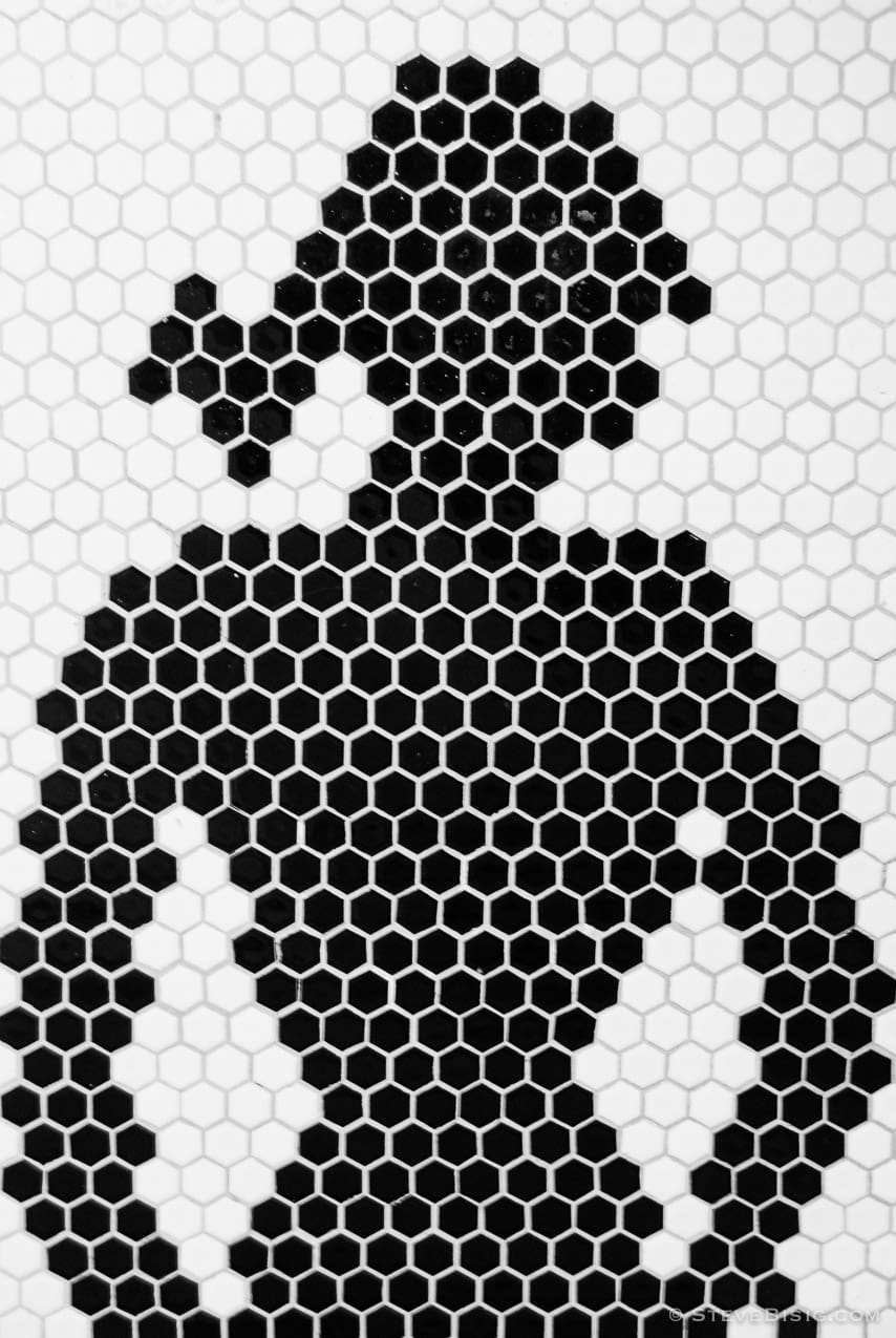 A black and white photograph of a mural of a woman made of hexagon tiles located outside the restroom at the Pike Place Market in Seattle, Washington.