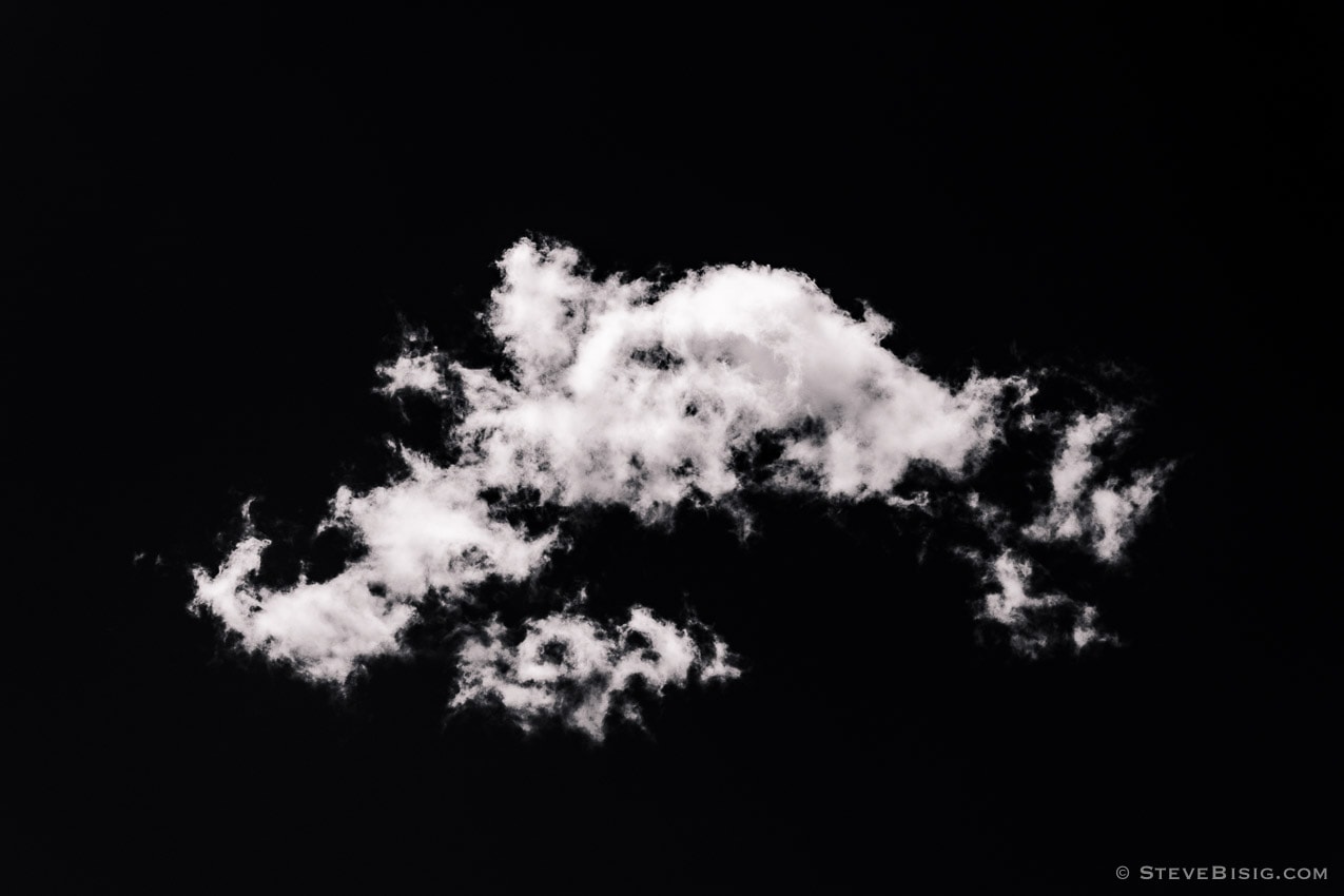 A black and white photograph of a lone cloud high over the Washington Cascade Mountains.