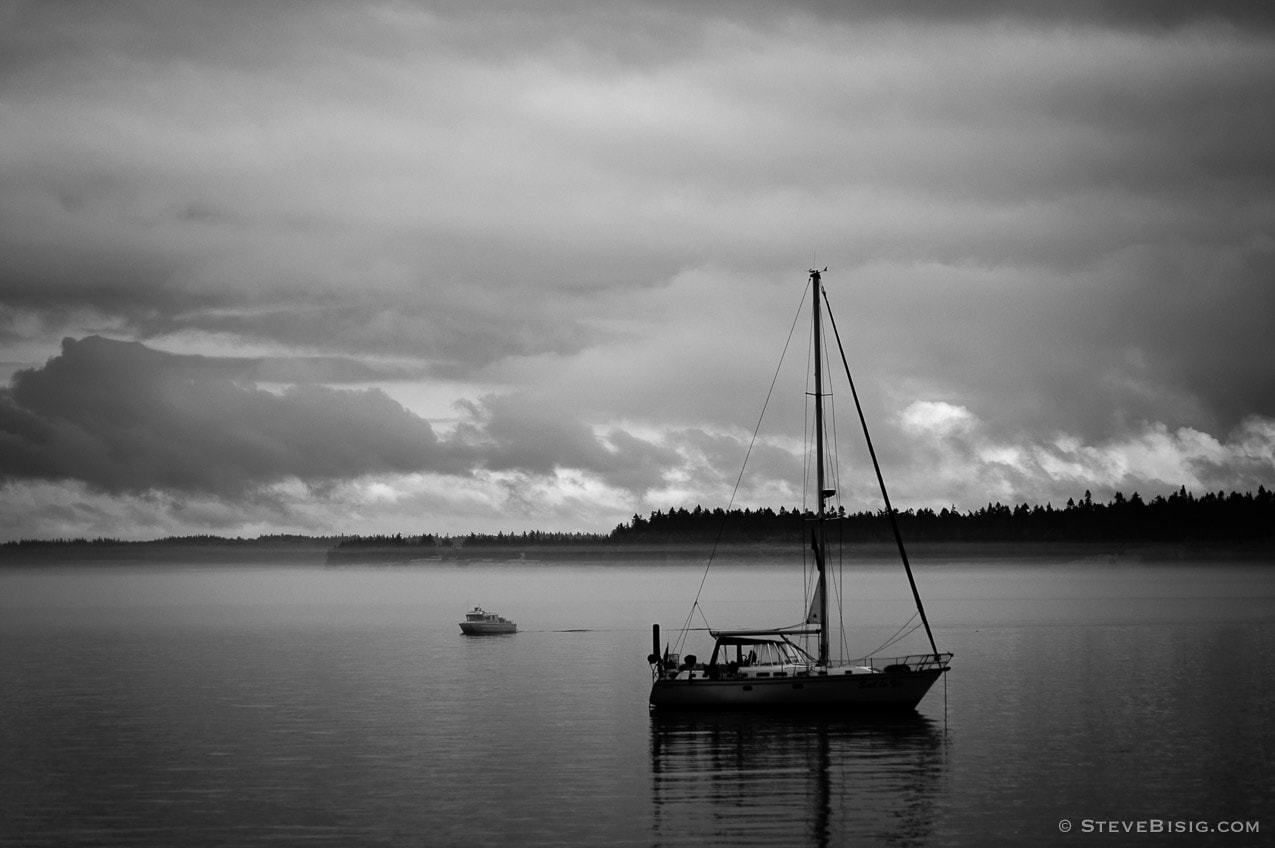 A black and white landscape photograph of a sailboat anchored offshore of Port Townsend, Washington.