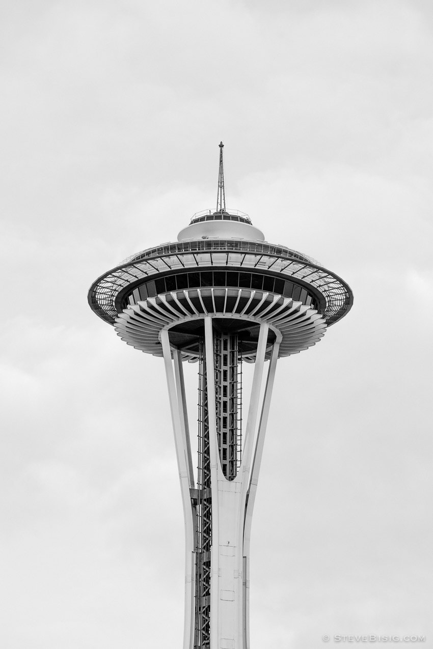 A black and white photograph of the upper section of the Space Needle as seen from the streets of Seattle, Washington.