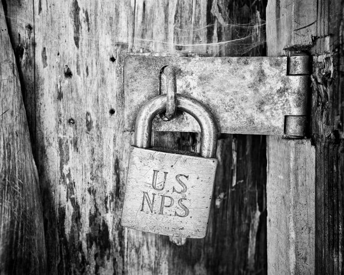 A black and white fine art cloe-up photograph of a well worn United States National Park Service pad lock and hasp that is secruring the door to the White River Patrol Cabin in the Mount Rainier National Park, Washington.